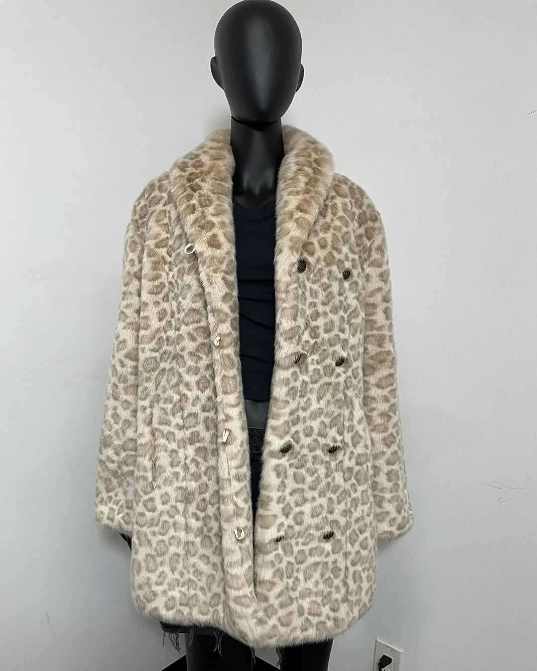 A beige and brown leopard-print faux fur coat with a wide collar, displayed on a black mannequin torso against a plain light gray wall.