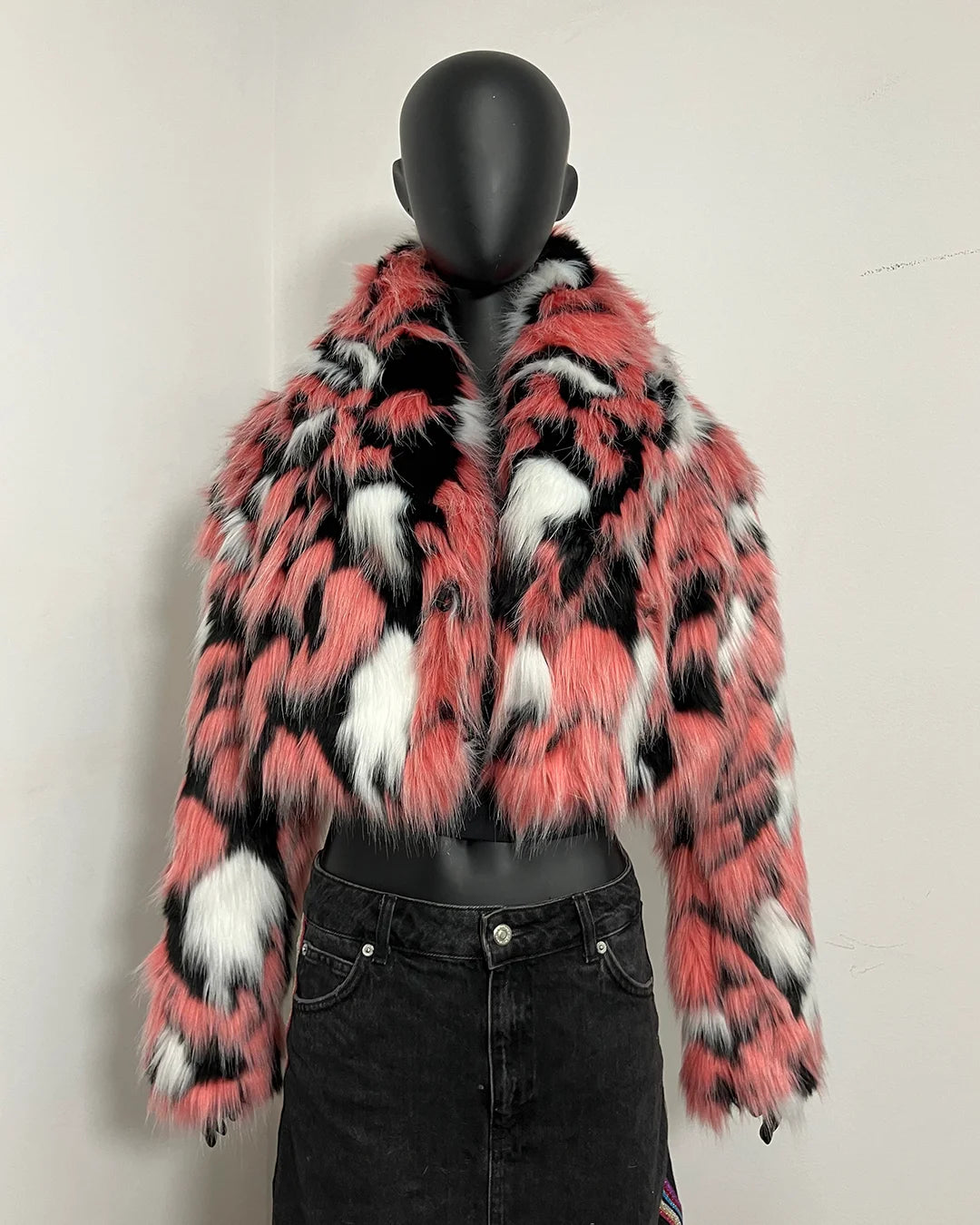 A cropped faux fur jacket with a bold pink, black, and white pattern, displayed on a black mannequin torso wearing a black denim skirt.