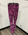 Pink leopard print leggings hanging on a black hanger against a white wall with a wood floor.