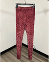 Red leopard print leggings hanging from a black plastic hanger against a plain beige wall and wood-look floor.