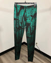Green patterned animal print leggings hanging on a black hanger against a plain indoor wall with wood flooring visible.