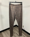 Brown and beige snakeskin print leggings hanging on a black hanger against a plain off-white wall with a wood-look floor.