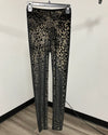 Black and beige leopard print leggings hanging on a metal hanger against an off-white wall and wood floor.