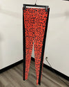 Bright orange and black leopard print leggings hanging on a black hanger against a white wall with wood flooring.