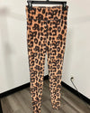 Leopard print leggings hanging on a black hanger against a white wall with a wood floor visible.