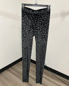 Black leopard print leggings hanging on a black plastic hanger against a plain beige wall and wood floor.