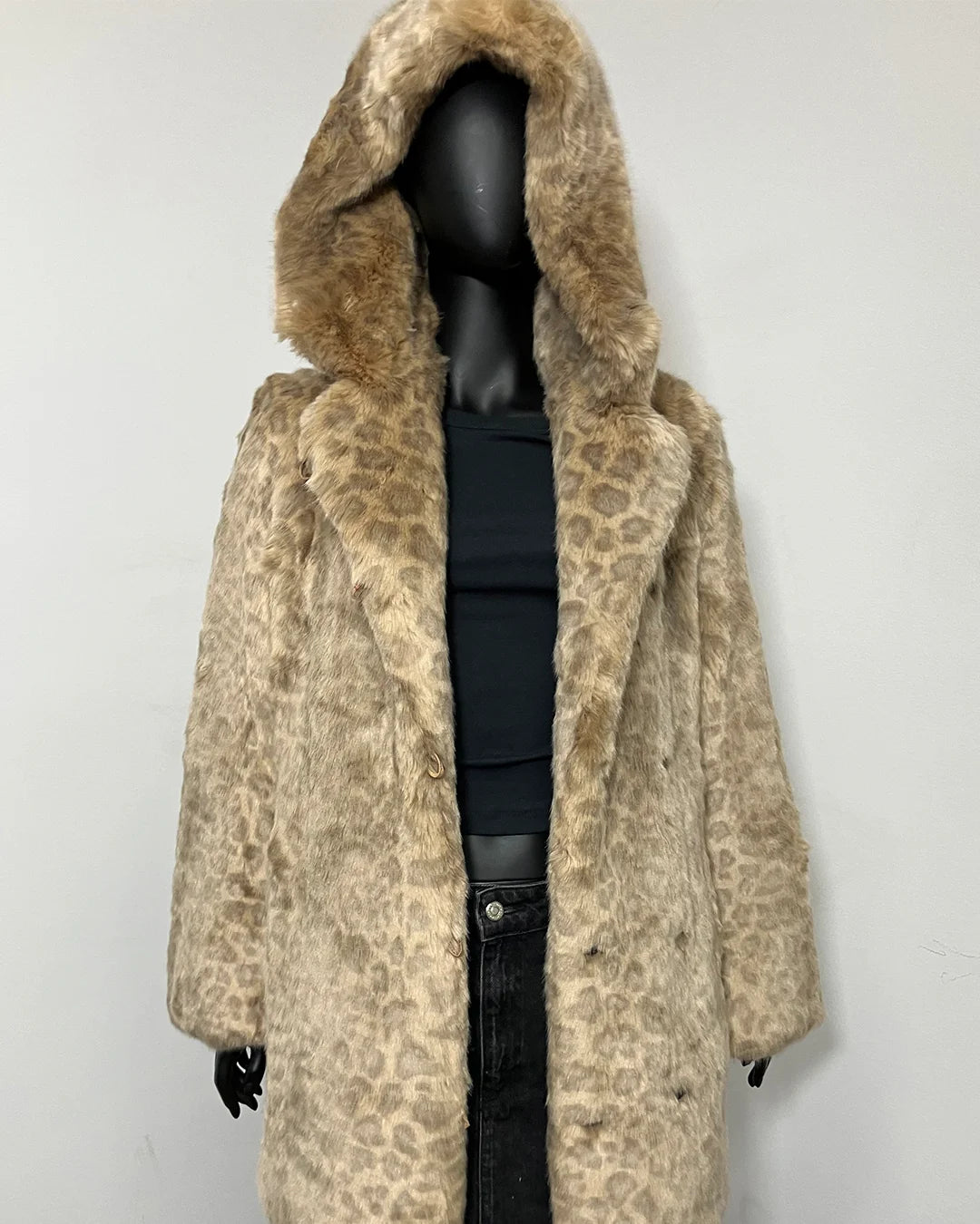 A beige and brown leopard-print faux fur coat with a large hood, displayed on a black mannequin against a plain light gray wall.