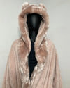 A plush hooded coat in a dusty blush pink faux fur material, featuring ear-like tufts on the hood and a black mannequin torso underneath, set against a plain light gray background.