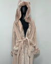 A plush faux-fur hooded robe in a light blush pink color, displayed on a black mannequin torso against a plain light gray wall.