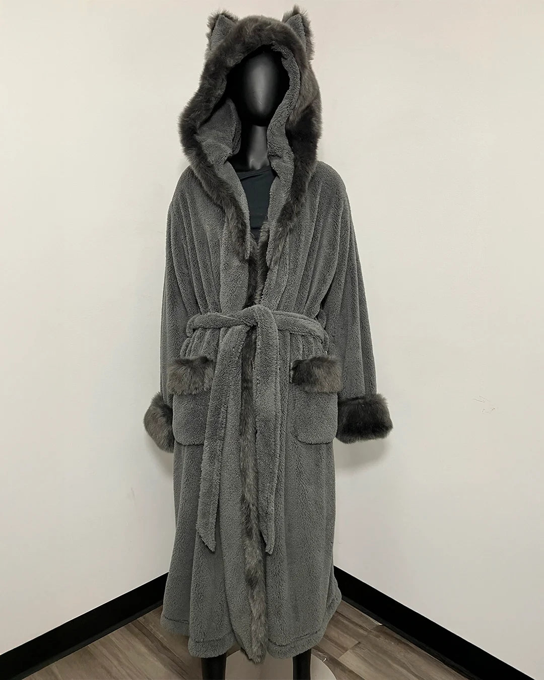 A gray plush hooded robe with faux-fur trim and ear-like details on the hood, displayed on a black mannequin against a plain white wall.