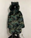 A long faux fur coat with a hood featuring cat-ear tufts, displayed on a black mannequin against a plain off-white wall. The coat has a mottled pattern of black, dark green, and olive-yellow.
