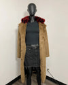 A long tan faux-fur coat with a bold red and black patterned fur collar, displayed on a black mannequin torso wearing a dark gray top and denim skirt against a plain white wall.
