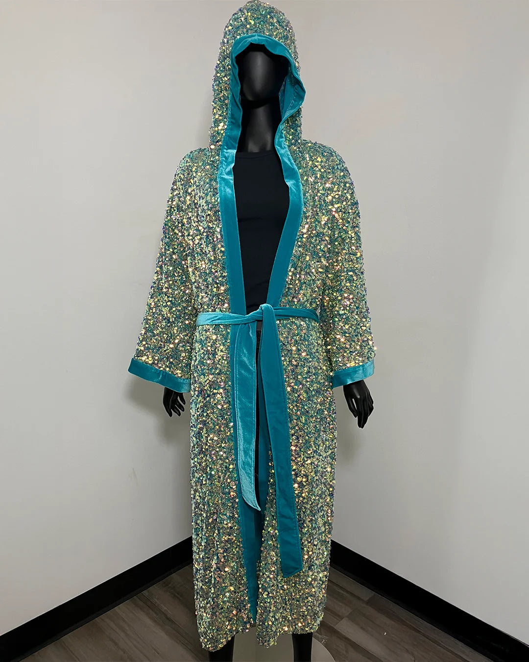 A hooded kimono robe with a dense multicolor sequin pattern and bright turquoise blue satin trim, shown on a black mannequin against a plain white wall.