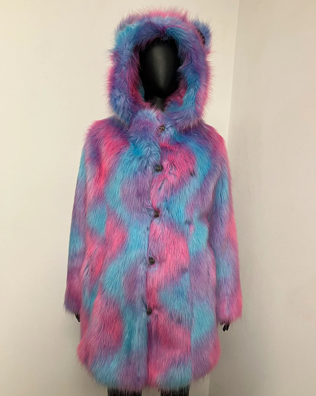 A hooded faux fur coat with a pink and blue tie-dye pattern, displayed on a black mannequin against a plain off-white wall.