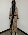 A hooded robe with a beige sequin floral pattern and black velvet trim, displayed on a black mannequin in a room corner.