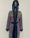 A hooded robe with multicolor sequins and dark blue velvet trim, displayed on a black mannequin against a plain light background.