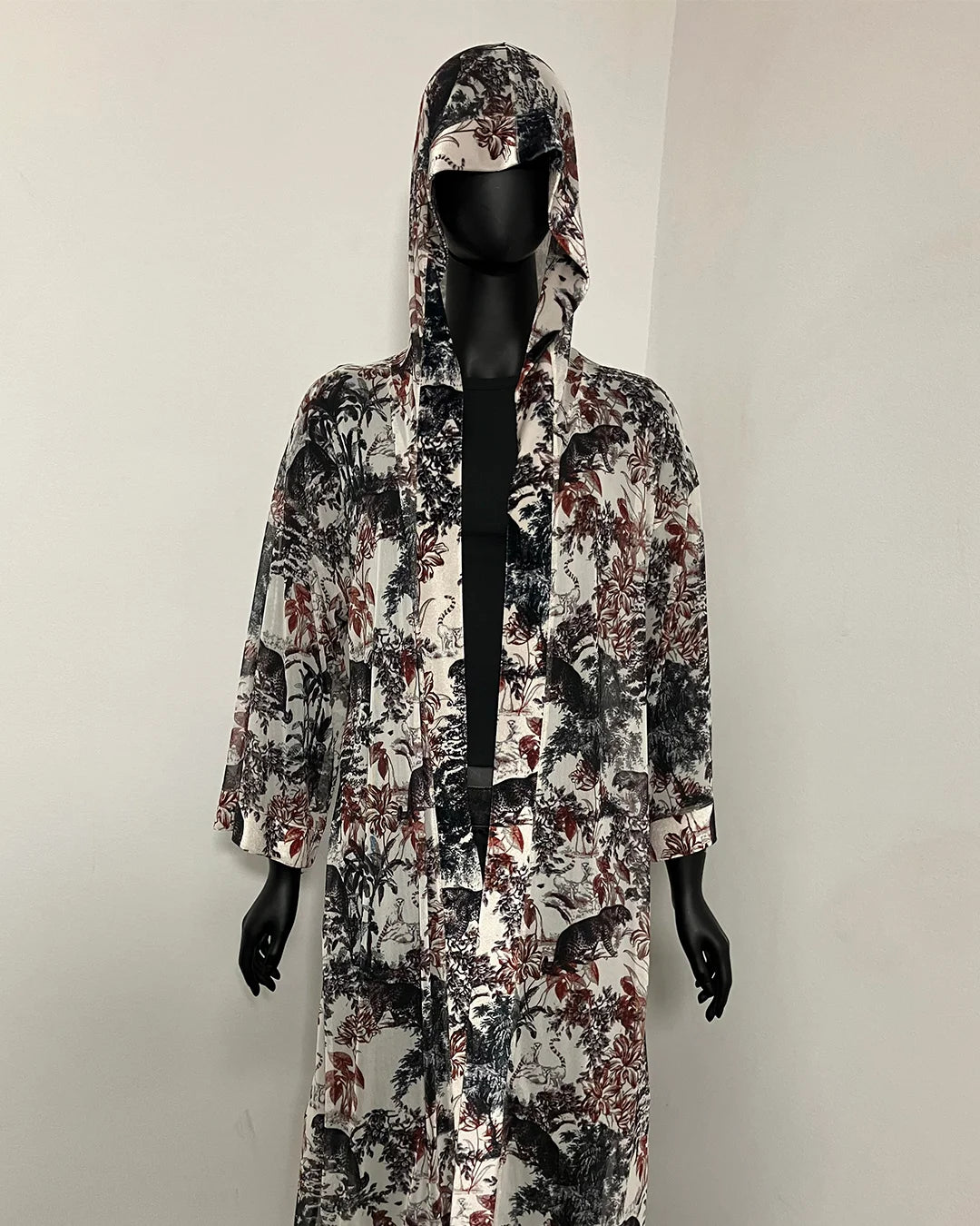 A hooded long-sleeve robe with an all-over abstract floral and botanical print in black, white, and muted red, displayed on a black mannequin against a plain light gray wall.