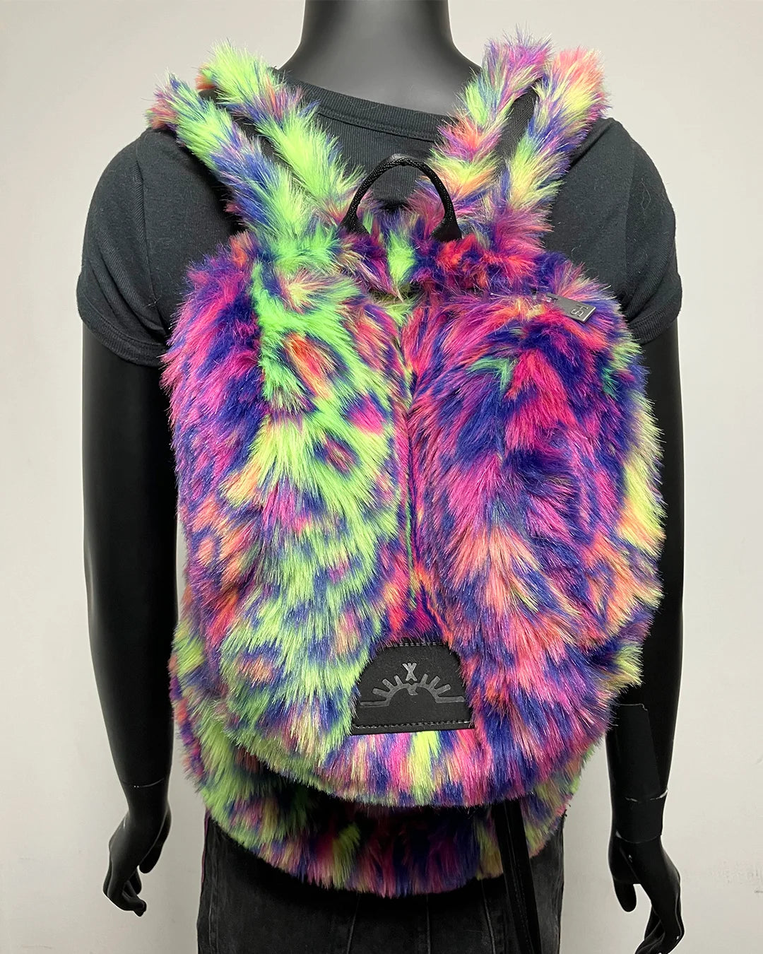 A multicolor fuzzy faux fur backpack with a tie-dye pattern of pink, purple, green, and yellow, displayed on a black mannequin torso. 