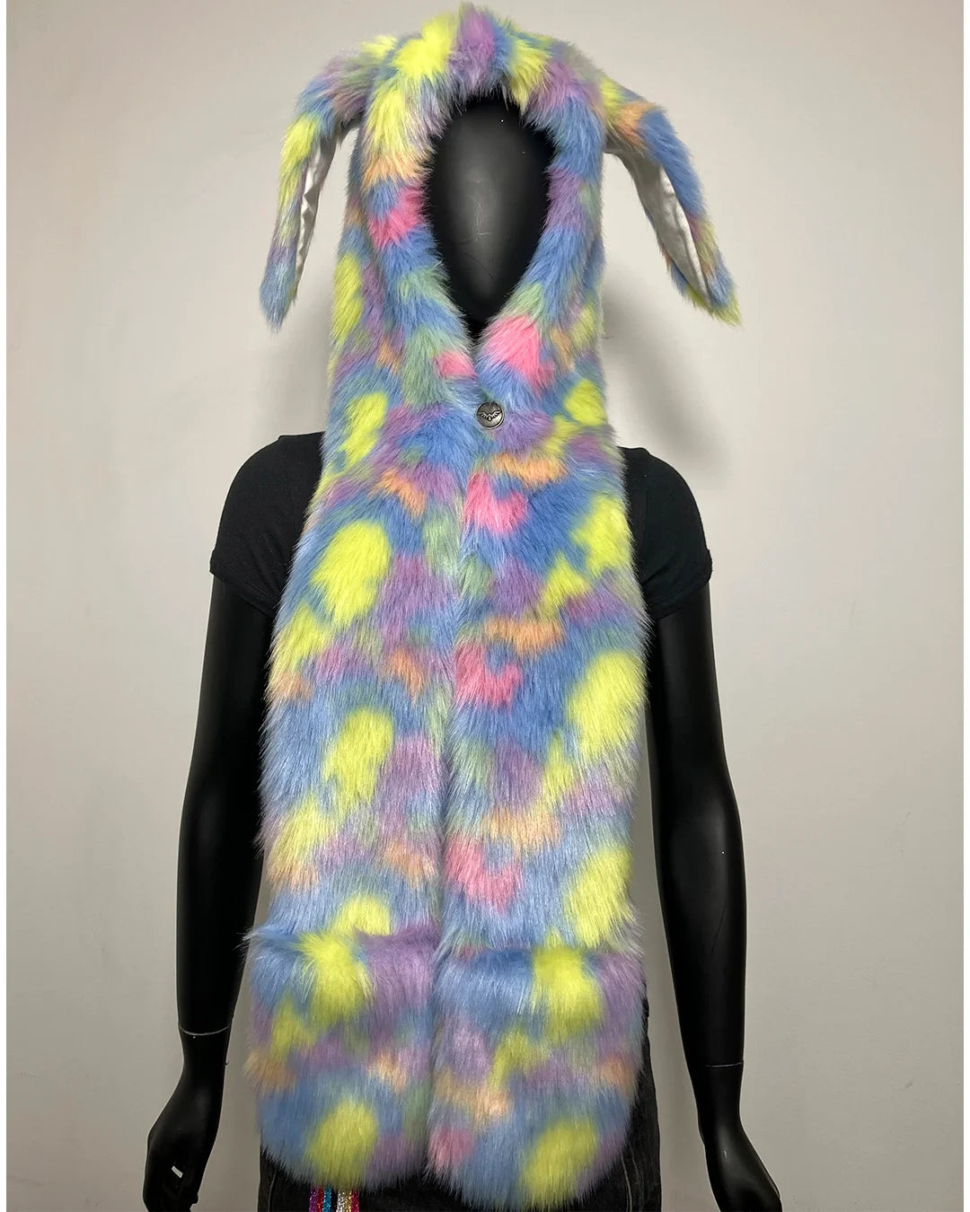 A faux fur festival hood with bunny ears, shown on a black mannequin against a plain light gray background. The vest has a pastel tie-dye pattern with blue, pink, yellow, and purple tones.