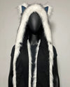 A festival hood with white faux fur trim and canine ears, displayed on a black mannequin. The hood has white Husky ears with blue inner lining, and the front has two blue paw-print pockets with purple gradient accents.