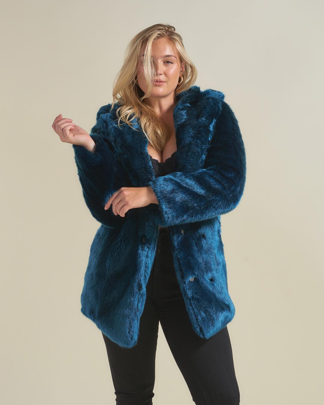A Woman smiling at the camera, wearing a SpiritHoods Royal Wolf Luxury Blue Faux Fur Coat with an oversized hood with ears, she is holding the sides of the hood while looking into the camera and smiling. 100% Fake Fur Coats for Women. Top Rated Womens Fall/Winter Faux Fur Coats and Clothing