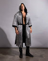 A man wearing a long, hooded kimono robe with a silver and black metallic snakeskin pattern, black lining, and a black waist tie, standing against a gray studio backdrop.