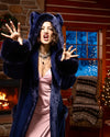 Model in a cabin that is decorated with christmas lights and a fire going in the fire place behind her, as she wears SpiritHoods Indigo Wolf Plush Luxury Robe, and does RAWR face. She has the plush hood up on the robe, showing the two wolf ears on the top of the hood.