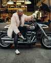 a Man on a motorcycle leaning forward, wearing spirithoods best selling pink faux fur jacket in pink flamingo. 100% Vegan Fashion Brand