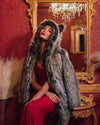 Woman in a SpiritHoods 100% Vegan Fake Fur coat and red dress sitting in a ornate room with a mirror and chandelier.