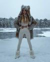 A Woman standing in Wonder Woman pose, looking out to the right, holding her hands at her waist as she stares into a winter wonderland, while wearing her plush SpiritHoods Arctic Fox 100% Vegan Fake Fur Coat  in a snowy landscape