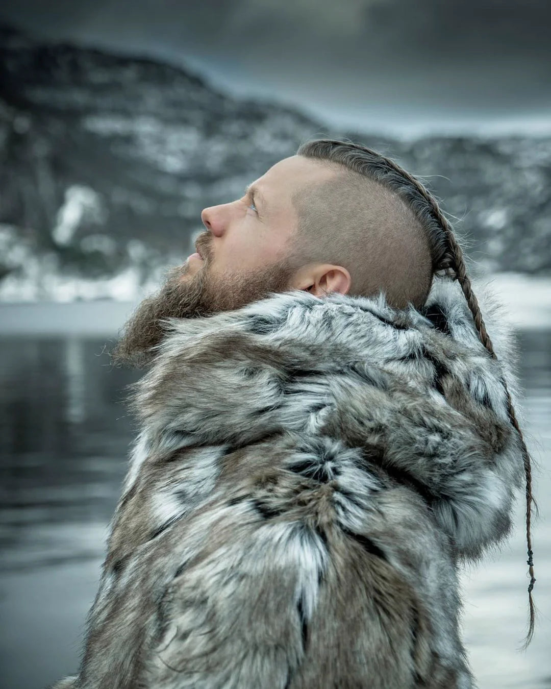 A man in the shadows, leaning against a pillar with one hand in his pocket, wearing a realistic fur Hooded Wolverine Coat.