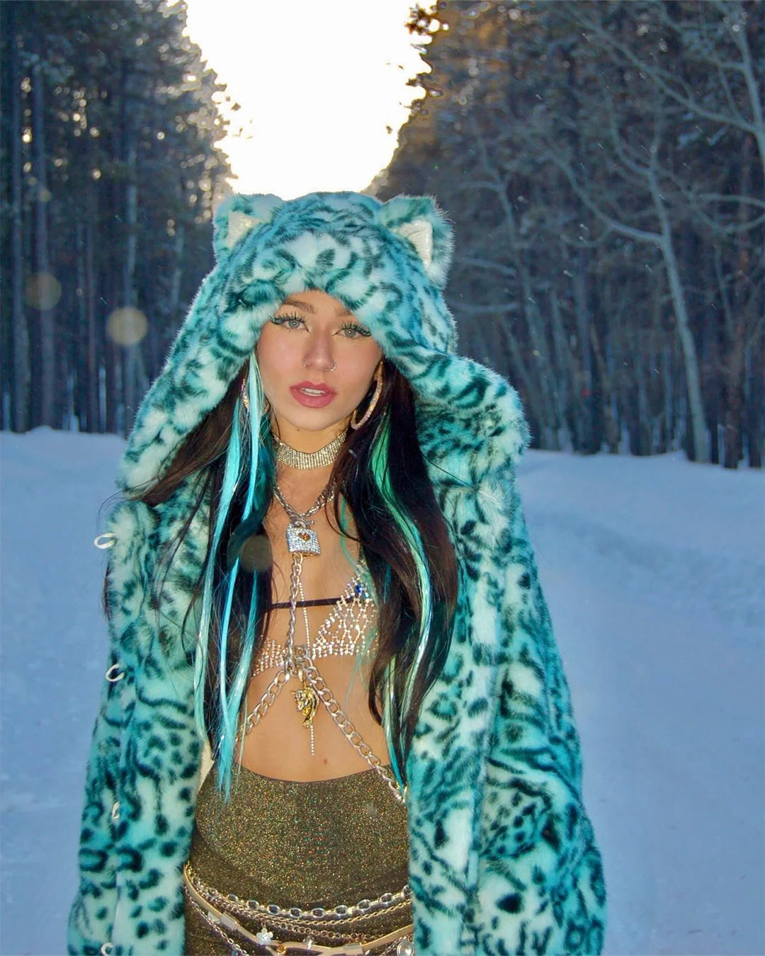 Model in the middle of the forest, with snow falling, wearing the SpiritHoods Aqua Cat Classic Collector Edition Faux Fur Coat, as she walks towards the camera 