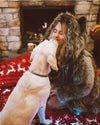 Woman in a Grey Wolf Classic Fake Fur Jacket by SpiritHoods sitting on a red christmas blanket with a dog, fireplace in the background