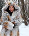 A Woman bundled up in the snow, wearing SpiritHoods Best Selling Arctic Fox Faux Fur Coat with ivory and golden fake fur  with a hood & ears in a snowy forest