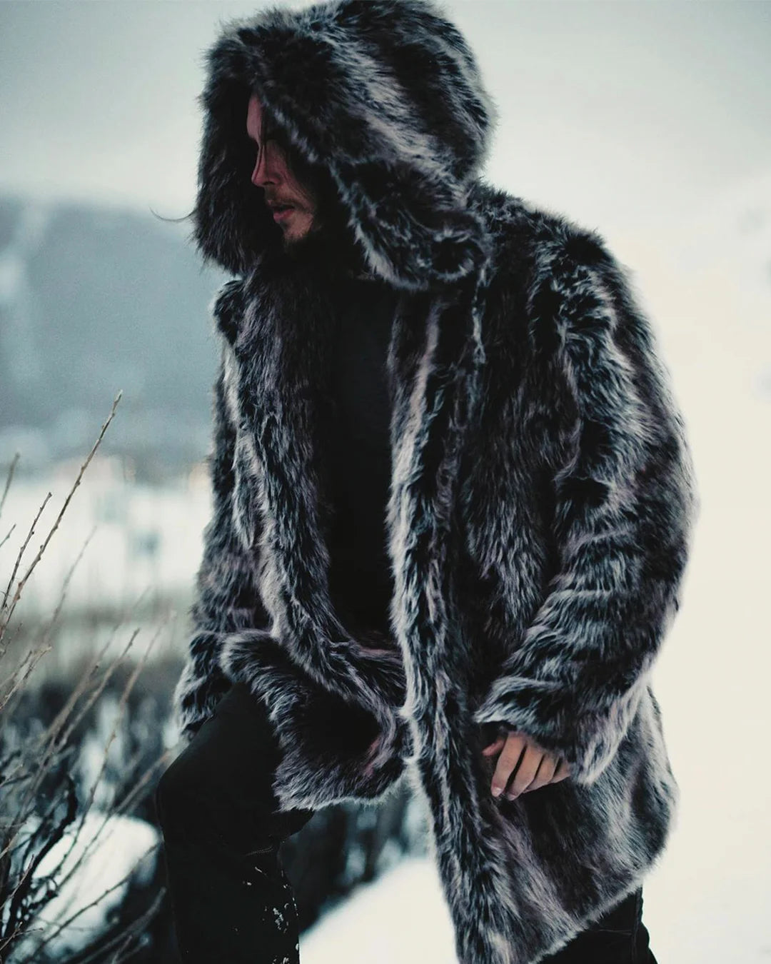 A Man wearing SpiritHoods Grey Wolf Hooded Faux Fur Coat in nature in the middle of winter and snow, walking up the mountains with the plush oversized hood on.