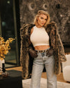 a model looking at the camera wearing jeans and  crop tank, with SpiritHoods Grey Wolf Faux Fur Coat drapped over shoulders getting ready for a holiday party with the girls