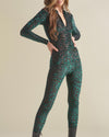 Side angle of woman with her hands on her hips wearing a green tiger print full-body bodysuit with a white background.