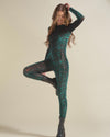 A woman doing a yoga pose wearing a green tiger print full-body bodysuit with a white background.