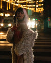 A Woman dressed as cruella deville, looking down, pretending to smoke, with street lights lit up behind her, as she crossed the street wearing SpiritHoods Long White Snow Leopard Print Jacket. Halloween Outfits, Halloween Costumes.