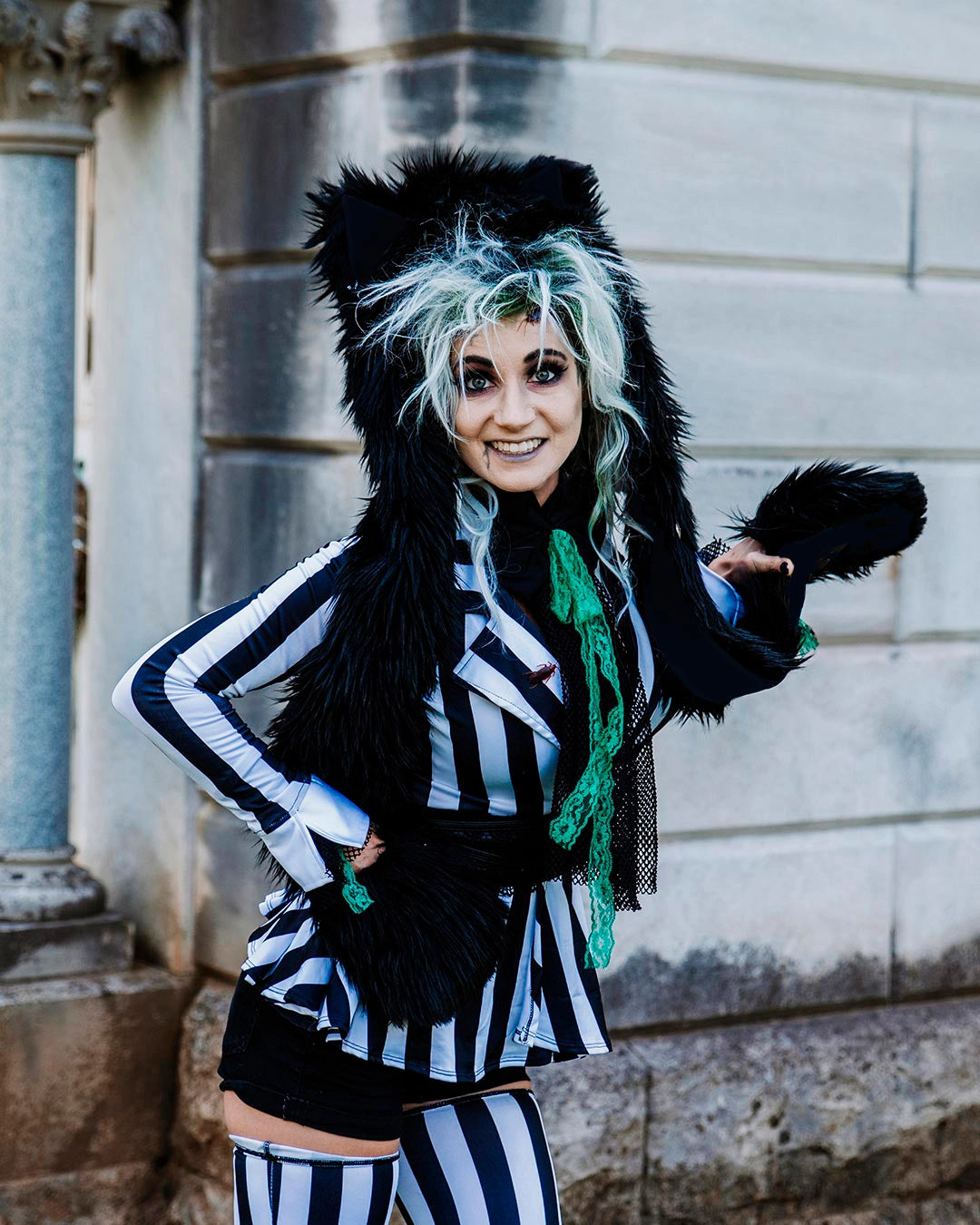 A Woman in a black and white stripped Beetlejuice inspired outfit wearing SpiritHoods Black Wolf Faux Fur Hood as she prowls through a cemetery. Easy Halloween Costume Ideas. Halloween Outfits for Women