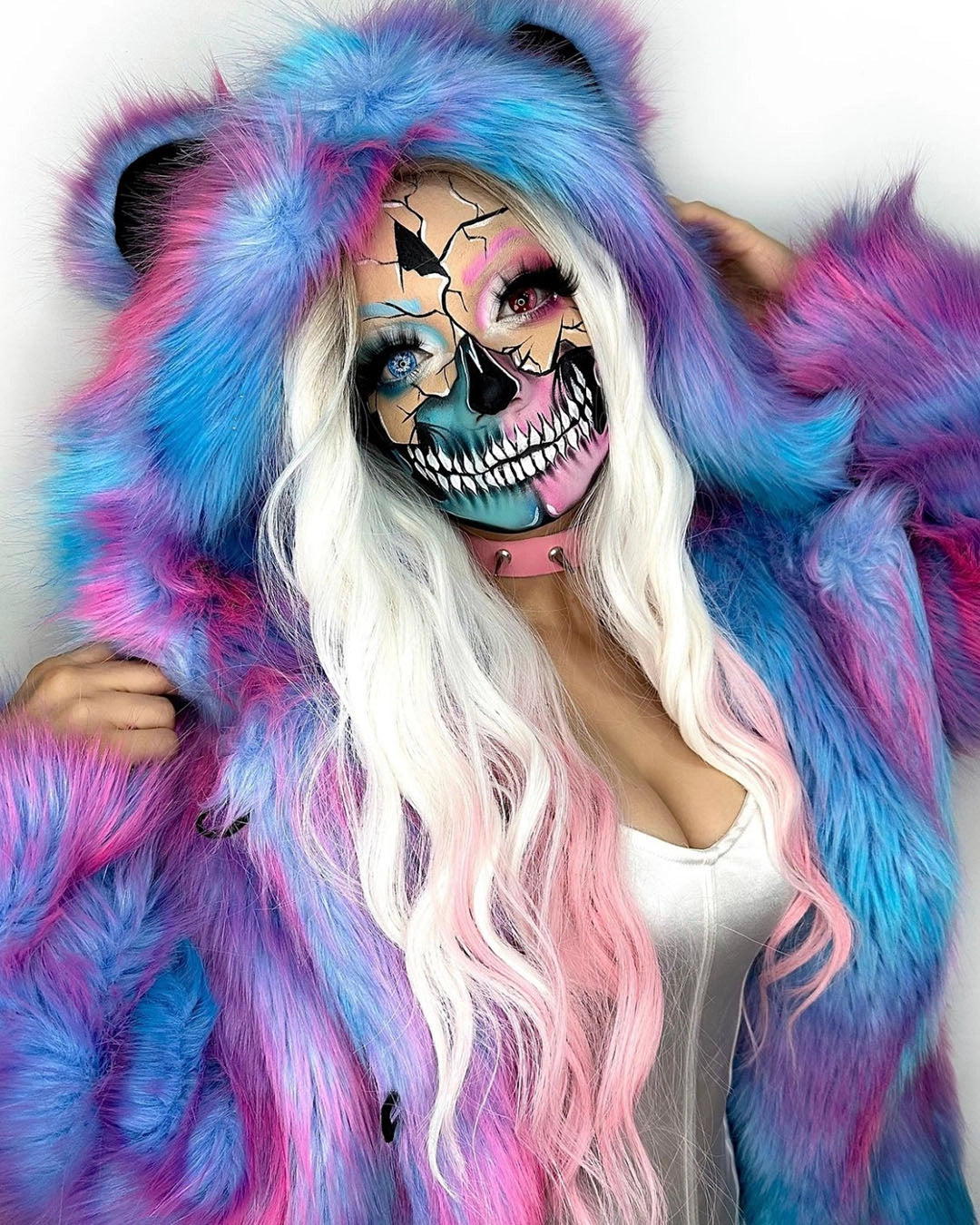 Woman wearing a colorful SpiritHoods Classic Cotton Candy Pink and Blue Tie Dye Faux Fur coat with a white background and blue and pink shattered skull make up. Halloween Costume Ideas Halloween Outfits
