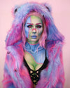 A Woman wearing a colorful tie dye pink and blue fake fur spirithoods coat with a pastel makeup comic-style face paint on a pink background. Halloween Make Up. Halloween Costume Ideas.