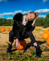 A Woman wearing SpiritHoods Black Wolf Hooded Fake Fur Jacket posing with a pumpkin in a field of pumpkins under a blue sky.