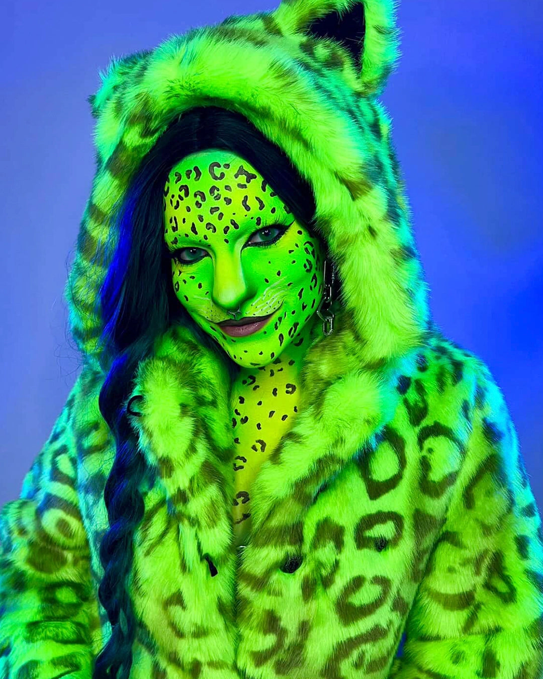 A Woman in Neon Green Make Up with Leopard Spots wearing SpiritHoods Neon Green Leopard Print Fake Fur Coat under UV Blacklight showing it glowing green. Halloween Costume Ideas. Halloween Outfits.