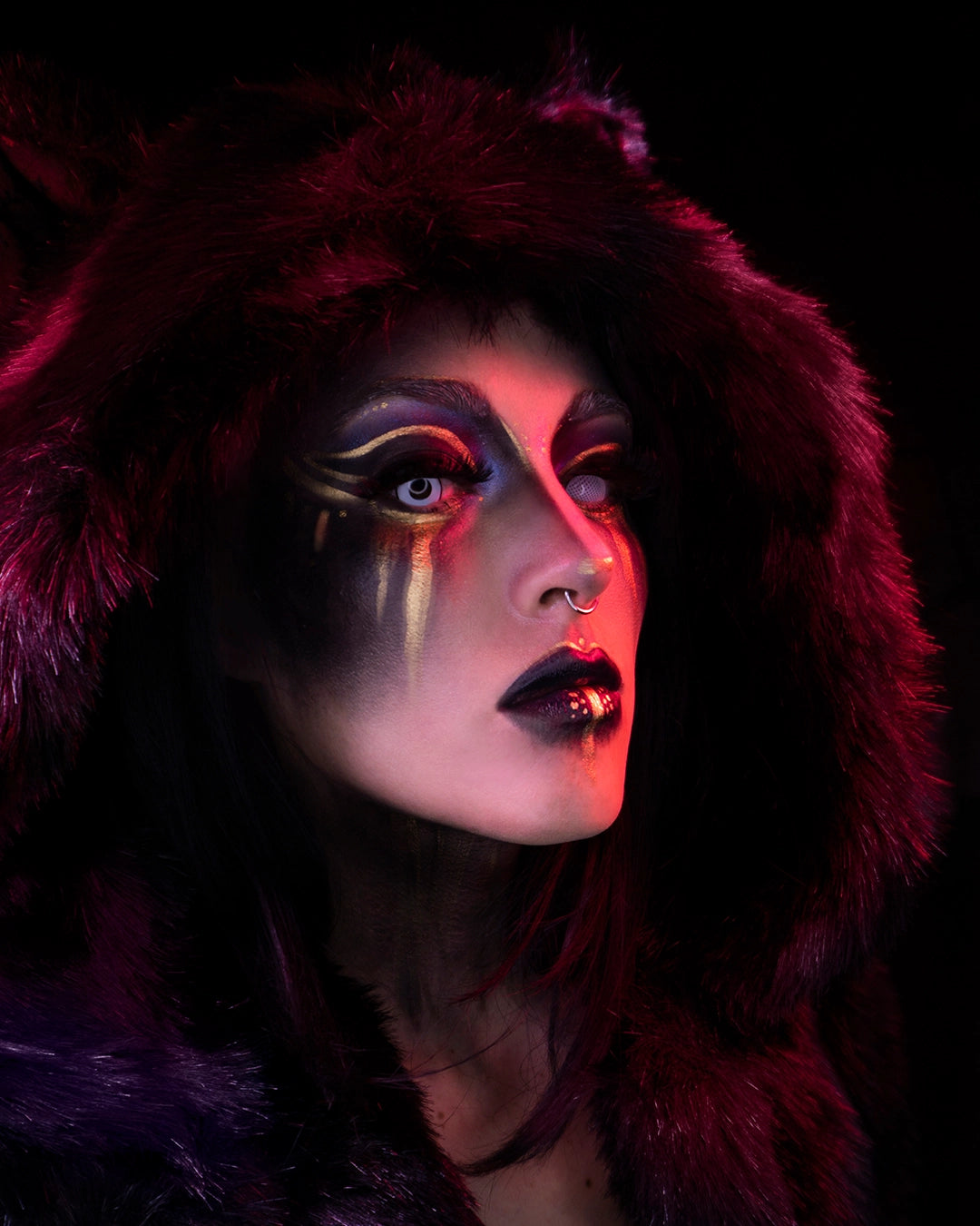 A Woman wearing SpiritHoods Black Panther Coat with the Hood Up looking at the camera with fake contacts in making her eyes white, with gold and black make up. Easy halloween make up ideas. Halloween Costumes and Outfits