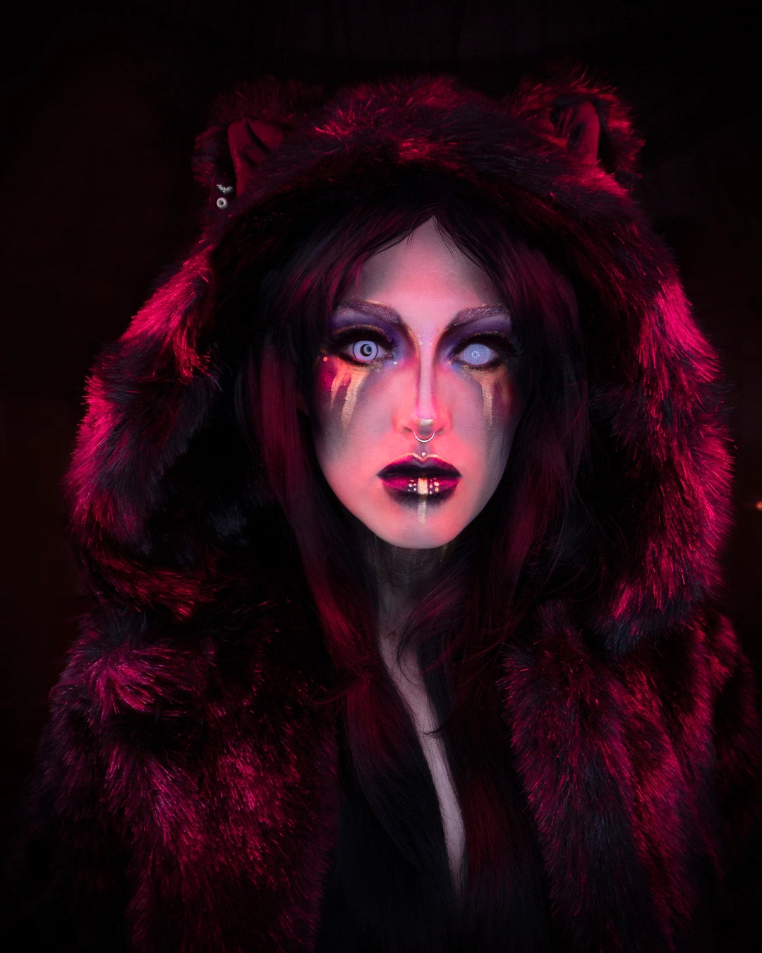 A Woman wearing SpiritHoods Black Panther Fake Fur Coat with white contact lenses in, looking at the camera with gold and black make up. The hood is up showing feline ears. Easy Halloween Make Up Ideas and Halloween Costumes.