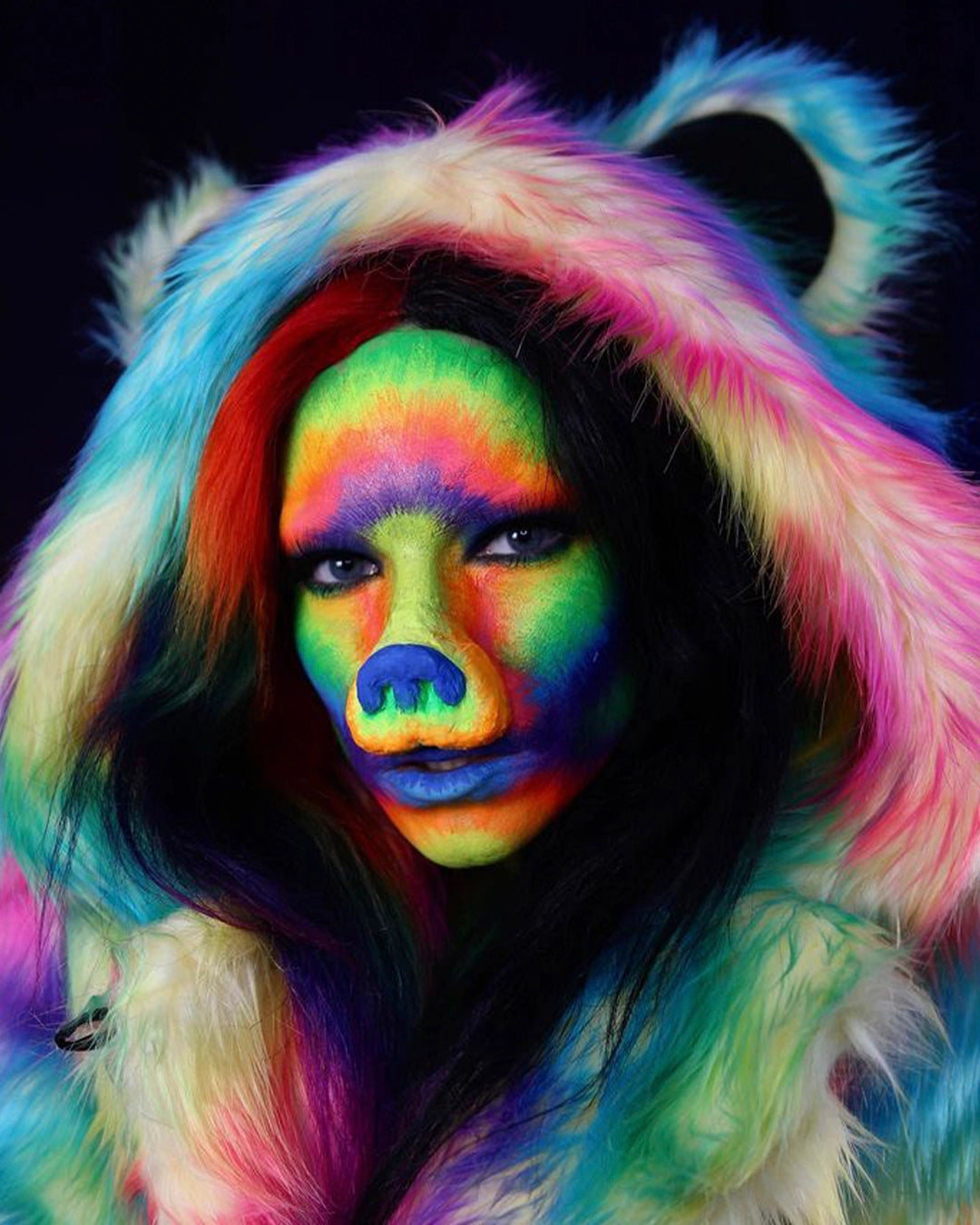 Woman wearing SpiritHoods Classic Rainbow Bear Faux Fur Coat with tiedye colors throughout, UV-blacklight reactive fake fur and face paint and bear nose. Halloween Costume Ideas. Halloween Make Up Inspiration.