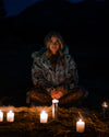 A Woman sitting in a dark outdoor setting with candles around wearing SpiritHodos Wolverine Fake Fur Hooded Coat and Black Lace Snakeskin Bodysuit underneath. Halloween Costume Ideas. Fall Fashion for Women and Witches