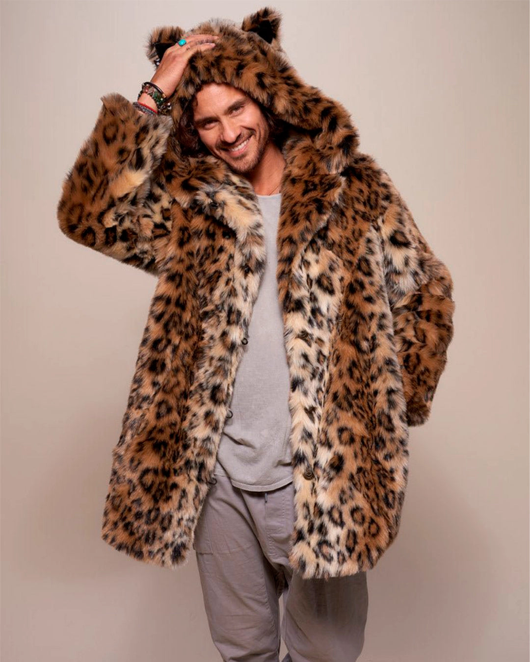 A Man smiling at the camera while wearing a leopard print faux fur coat with a hood on a plain background. SpiritHoods Made to Order Fall Winter Coat Collection. 100% Fake Fur Custom Made Jackets for Men