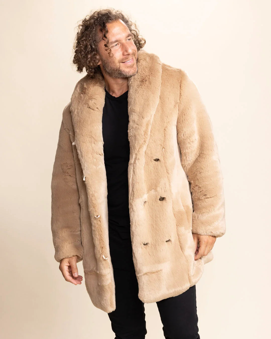 Man wearing a beige faux fur SpiritHoods Cougar coat against a plain background, looking over his shoulder, smiling, feeling confident in his fresh layers.